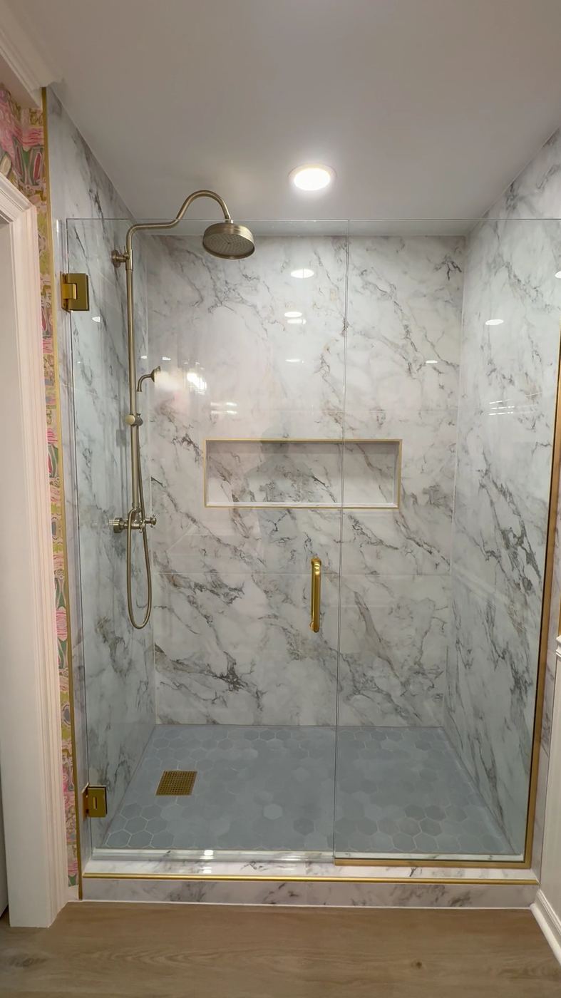 Marble-look tile shower with a brass-framed glass door